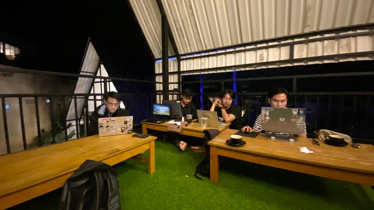 Four people working on laptops at wooden tables on an outdoor terrace at night